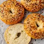 Protein Bagels: The Best 30g High-Protein Bagels You’ll Love 6 Golden brown protein bagels in a basket with one sliced and spread with cream cheese on a breakfast table