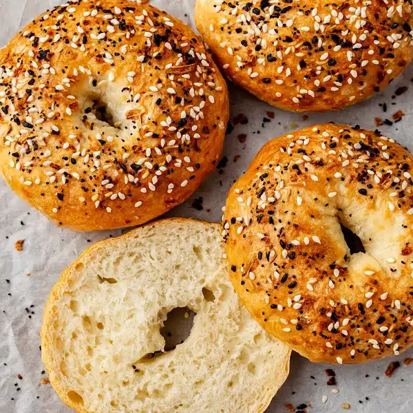 Best Protein Bagels Recipe Hub– Family-Approved 12 Golden brown protein bagels in a basket with one sliced and spread with cream cheese on a breakfast table