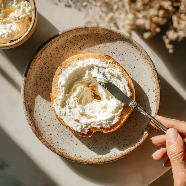 5 Healthy High-Protein Bagel Toppings That Actually Keep You Full 22 hand spreading ricotta cheese on bagel as base for sweet toppings