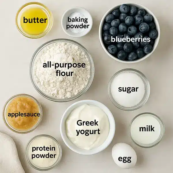 Blueberry Protein Muffins: 9g Protein, Irresistible Snack You’ll Love 7 Labeled ingredients for blueberry protein muffins on a white marble counter.