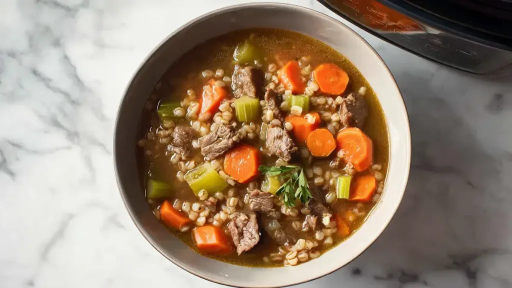 Bowl of beef barley soup with carrots, celery, and tender beef chunks on a marble background