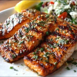 Plate of perfectly grilled salmon fillet garnished with herbs and lemon