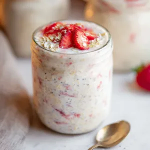 High-protein strawberry cheesecake overnight oats in a glass with fresh strawberries.