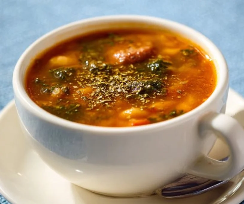 Bowl of Mediterranean kale and white bean soup with sausage garnished with herbs.
