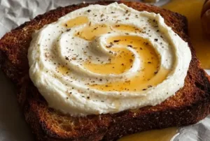 Whipped ricotta toast with honey, garnished with fresh herbs and edible flowers.