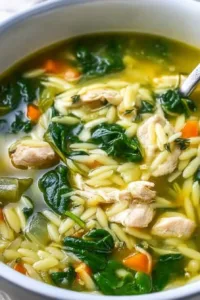 Bowl of Lemon Chicken Orzo Soup garnished with herbs and lemon slices.